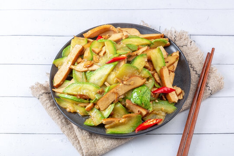 成品菜肴特写:洁白茭白片与紫红色洋葱条交错排列,表面泛着油亮光泽,点缀绿色葱花,盛放在白色瓷盘中,背景虚化的餐桌上有米饭和筷子 图片描述