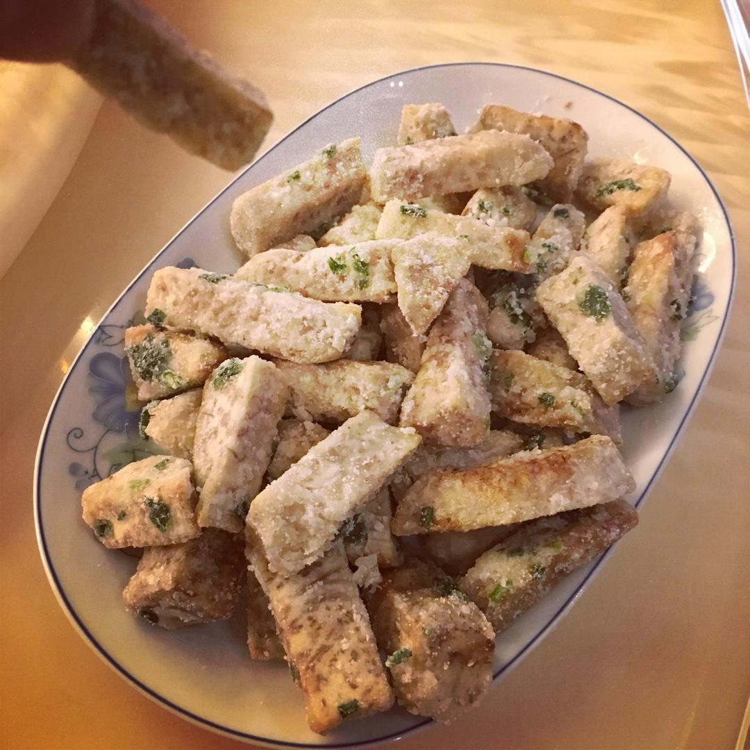 拔丝荔浦芋头制作过程特写：金黄酥脆的芋头条整齐铺在不锈钢漏网中沥油，背景为高温油锅泛起细密气泡