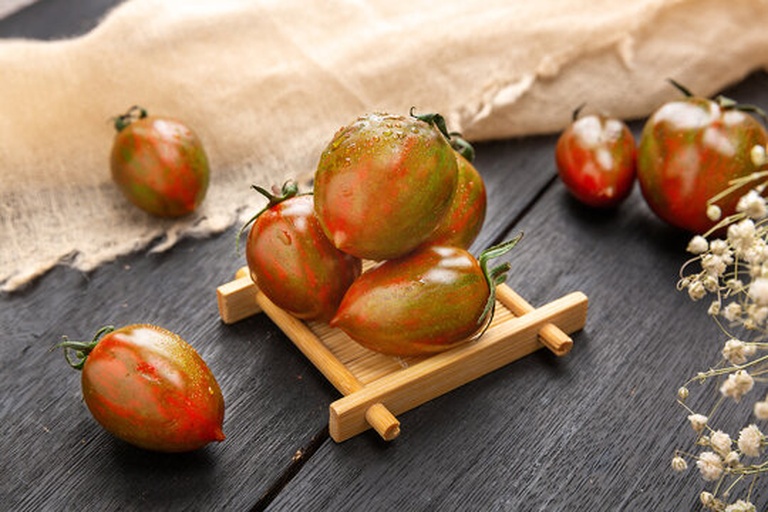 一盘红色圣女果与一个切开的普通大西红柿并列摆放,背景为木质餐桌,光线柔和,突出两者在大小、形状和色泽上的差异 圣女果与普通西红柿对比图