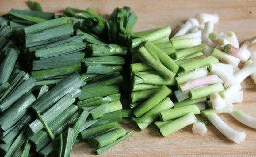厨房场景：不锈钢砧板上切好的韭菜段与香菜碎混合，旁边摆放玻璃碗盛装芝麻香油、蒜末、少许生抽，体现安全合理的家常搭配方式