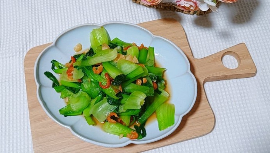 高清俯拍:青翠油菜茎叶分明,虾皮呈金粉色均匀点缀其间,表面泛琥珀色油光;盘底无水渍,油菜根部微翘显脆度;背景为原木砧板与青瓷浅盘,突出食材本真质感 虾皮油菜出锅装盘特写
