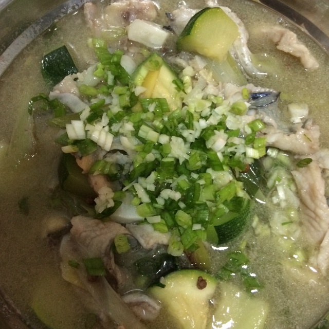 一锅正在炖煮的浅白色鱼汤,汤中可见整段西兰花茎叶与鱼块共同炖煮,表面浮有少量油星,旁边摆放新鲜西兰花和去鳞清洗干净的整条鲈鱼,背景为厨房灶台,体现家庭烹饪场景 西兰花与清炖鱼合炖的成品菜肴