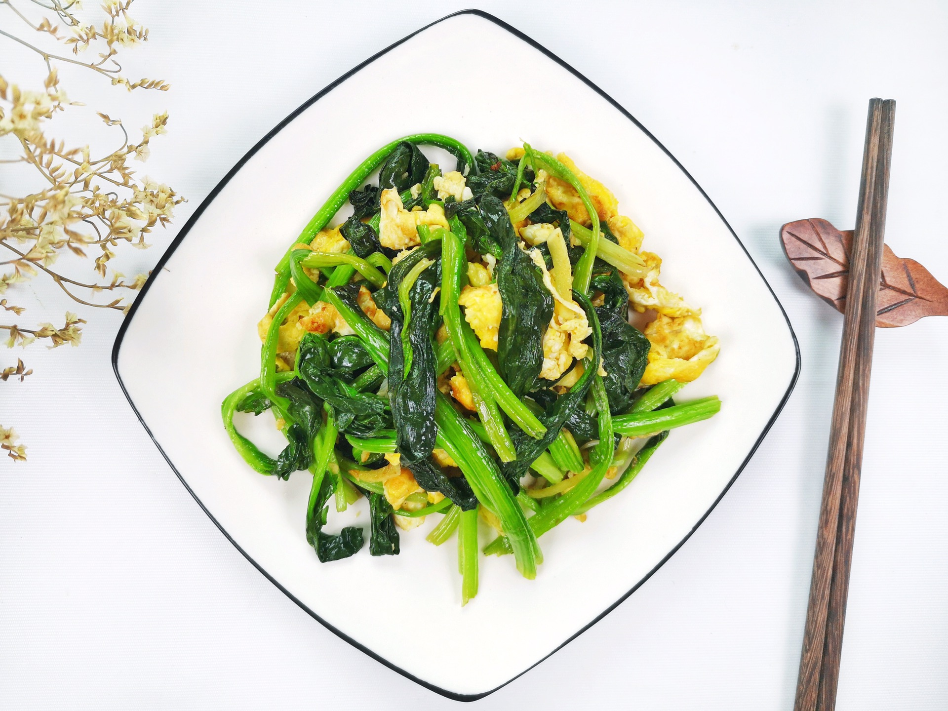 一盘刚出锅的菠菜炒鸡蛋平铺在白色圆盘中,金黄的鸡蛋块与翠绿的菠菜交错分布,表面泛着油光,旁边摆放一双木筷,背景虚化 成品菠菜炒鸡蛋特写