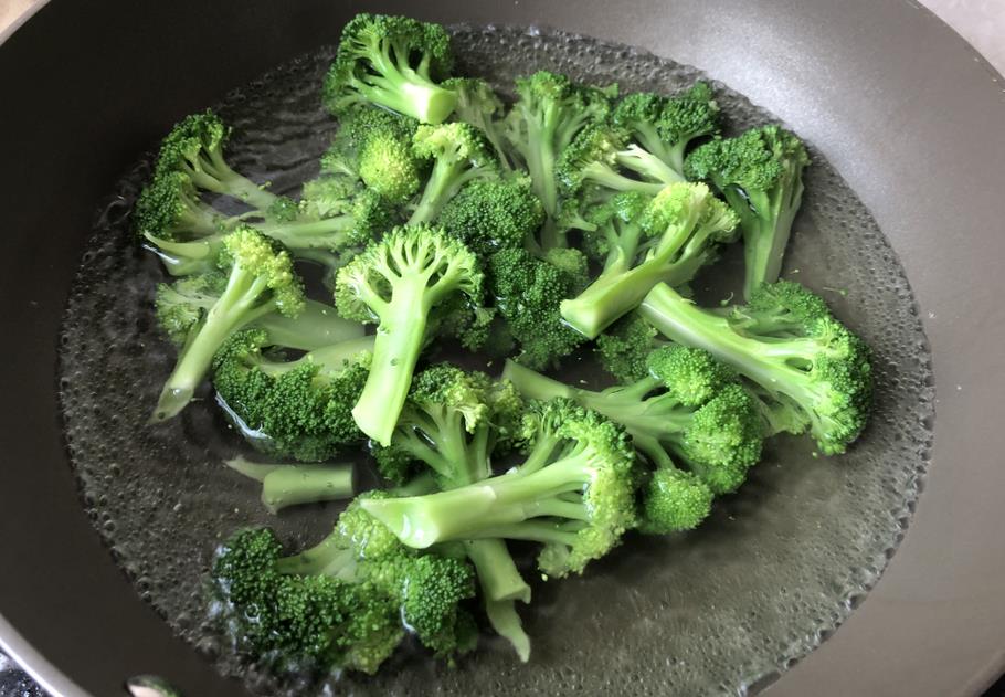 一名厨师正在用不锈钢锅焯煮西兰花,锅中水沸腾,西兰花呈亮绿色,旁边配有蒜瓣和橄榄油,台面上有盐罐和木勺,展示健康烹饪场景 西兰花烹饪过程
