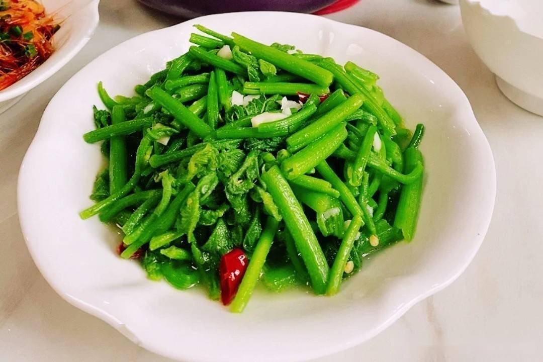 一盘清炒南瓜藤尖摆放在木质餐桌上,菜肴色泽翠绿,搭配蒜末点缀,旁边放有一双竹筷和一个小瓷碗,整体呈现家常健康饮食风格 图片描述