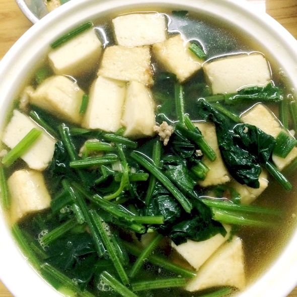 一盘新鲜绿叶菠菜与蒸熟的豆包并列摆放,背景为厨房台面,左侧为洗净的整株菠菜,叶片翠绿肥厚;右侧为白色蒸笼中的两个圆形豆包,表面微黄有光泽,散发热气,体现家常健康饮食氛围 菠菜与豆包食材对比图