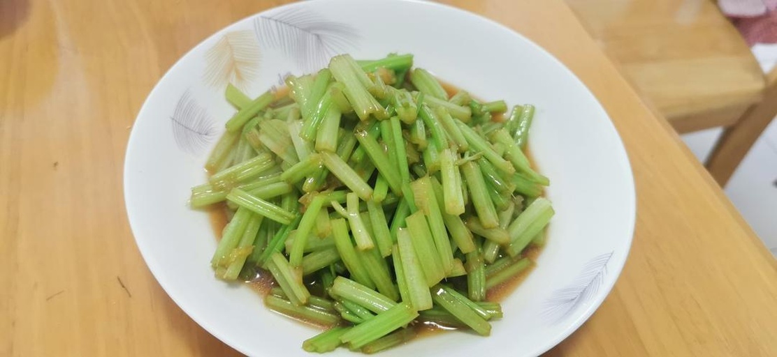 中式家常炒芹菜出锅特写：翠绿色芹菜段与金黄鸡蛋块相间，点缀几粒红椒丁，油亮诱人，热气微升，盛于青花瓷盘中，展现传统健康家常菜风貌