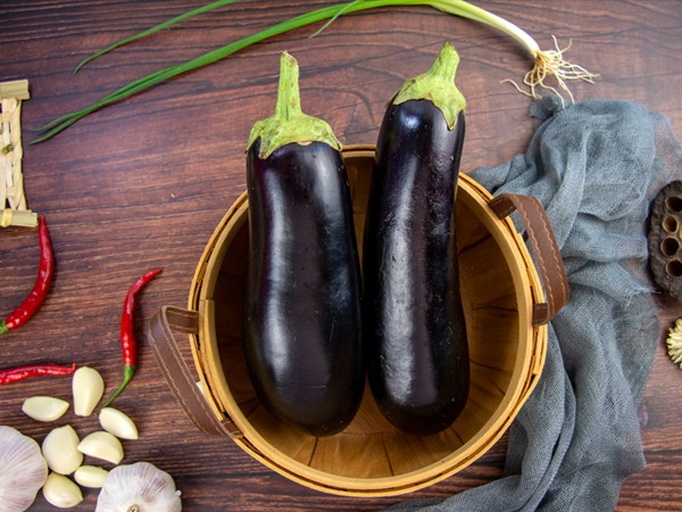 厨房操作台上摆放着新鲜的猪排骨、紫色长茄子和黄色土豆,旁边有生姜、大蒜、葱段、八角等香料,背景为木质砧板和刀具,光线柔和,突出食材的新鲜感与自然质感 图片描述