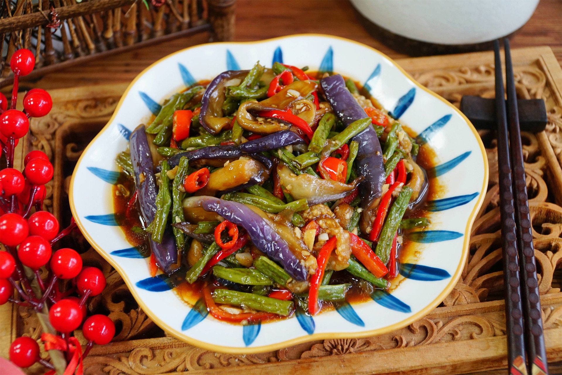 一道色泽油亮的毛豆米烧茄子被盛放在圆形白色瓷盘中央,茄子呈深褐色,毛豆米翠绿醒目,表面点缀着红色辣椒圈和葱花,旁边配有米饭和竹筷,整体摆盘整洁美观,灯光柔和 成品毛豆米烧茄子盛在白色瓷盘中