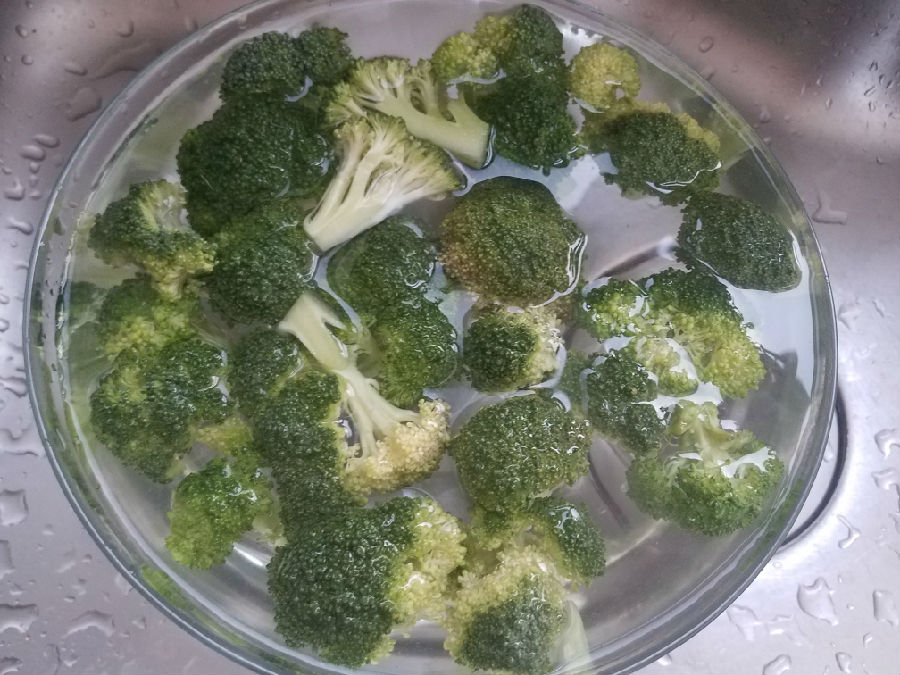 厨师正在将焯好的西兰花投入冰水中冷却，旁边摆放着切好的梨条浸泡在透明玻璃碗中