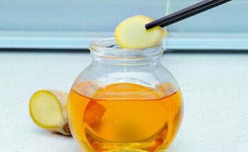 一瓶透明玻璃罐中装有橙黄色的姜蜜膏,质地浓稠均匀,表面光滑反光,瓶盖拧紧,放置在铺有麻布的桌面上,旁边摆放一柄木制小勺,背景可见新鲜生姜块和蜂巢片段 姜蜜膏成品展示图