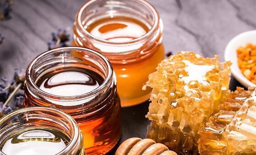 一罐天然蜂蜜特写,背景为蜂巢与蜜蜂,突出蜂蜜的自然来源与纯净质感 蜂蜜特写