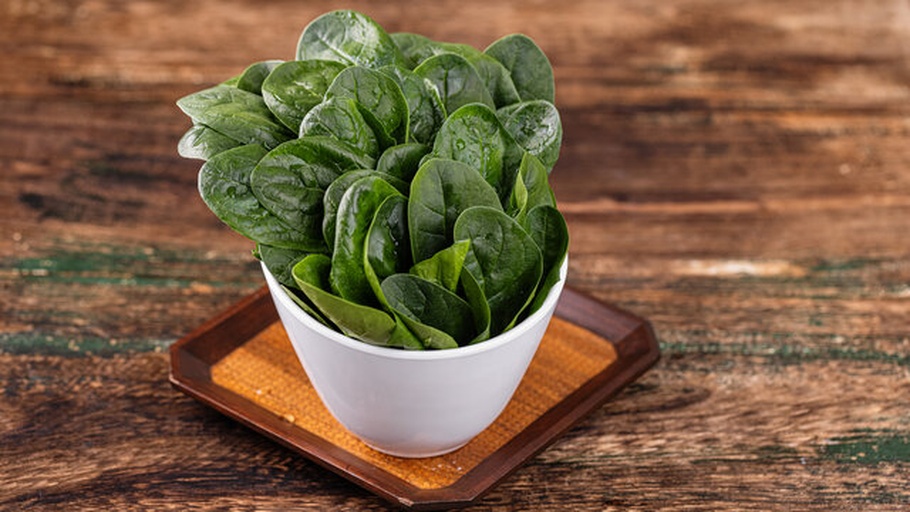 一张木质餐桌上,左侧是一盘焯水后的深绿色菠菜拌芝麻,右侧是一碗混合生菜沙拉中的浅绿色嫩菠菜叶,旁边配有柠檬片和橄榄油瓶,自然光线明亮 厨房中摆放两盘不同颜色的菠菜菜品