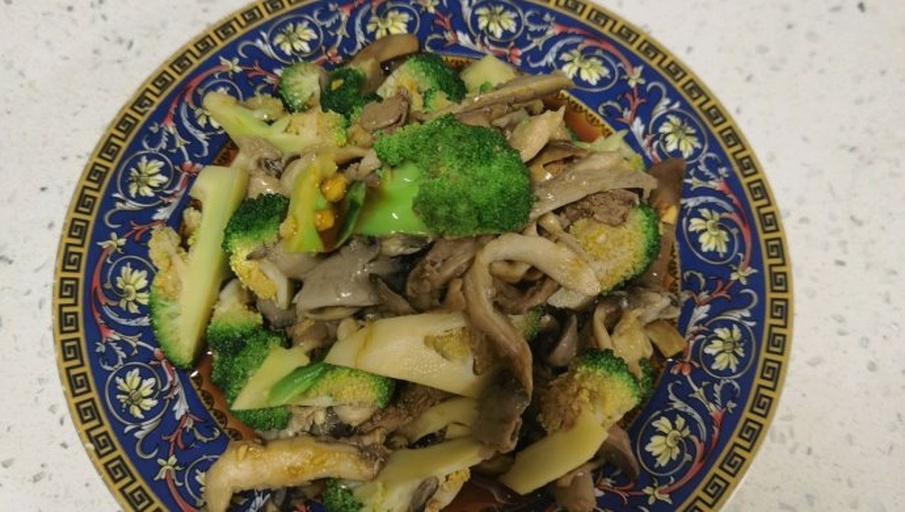 成品展示：一盘色泽鲜亮的西兰花炒杏鲍菇，盛于浅灰色陶瓷盘中，旁边配有米饭和竹筷，背景柔和温馨