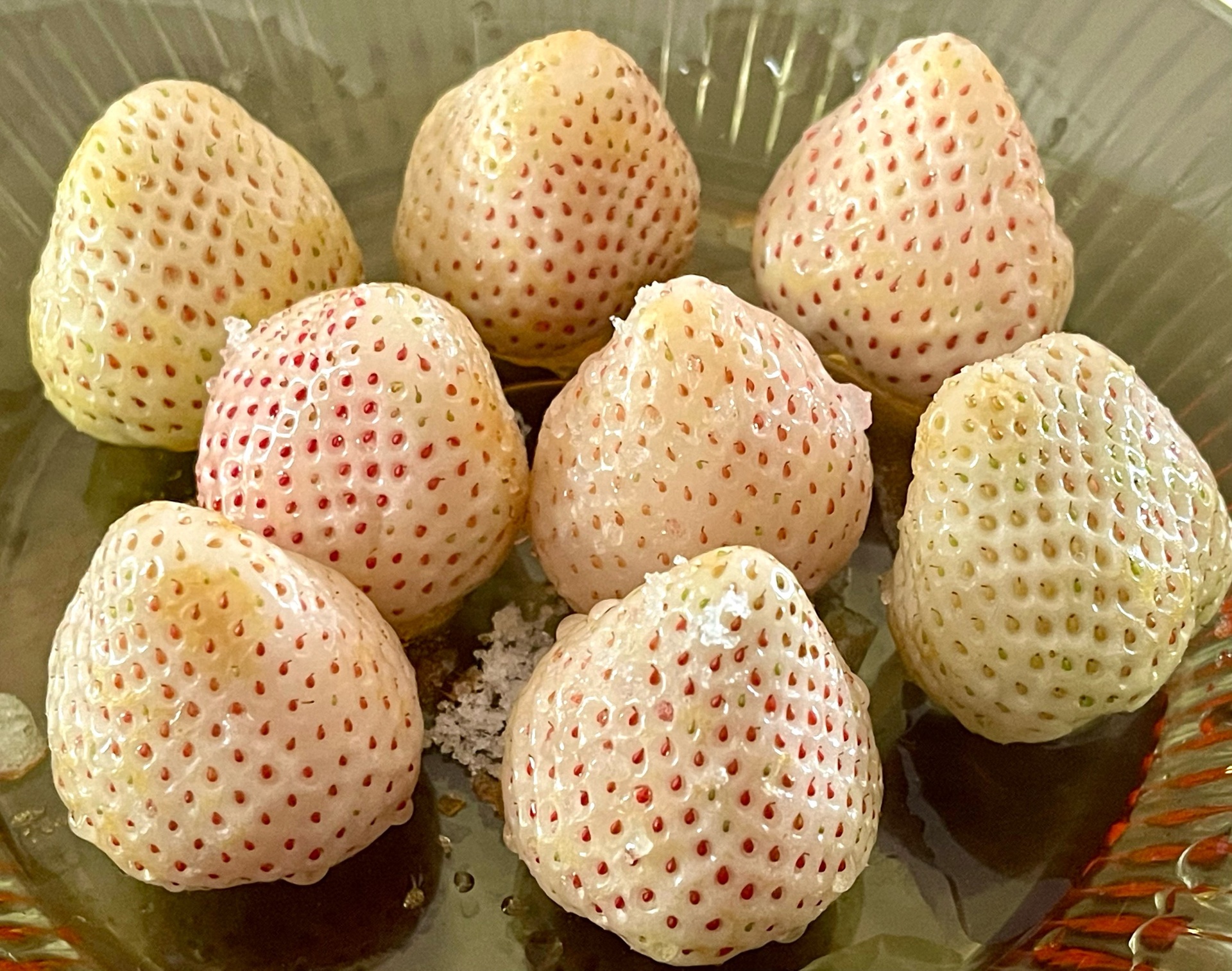 一位厨师正在光线充足的厨房中,手持一颗乳白色的阿尔卑斯白草莓,仔细观察其表皮色泽与果蒂状态。旁边摆放着几颗不同成熟度的白草莓作为对比,背景有放大镜和食品级手套,突出专业挑选过程 挑选新鲜阿尔卑斯白草莓