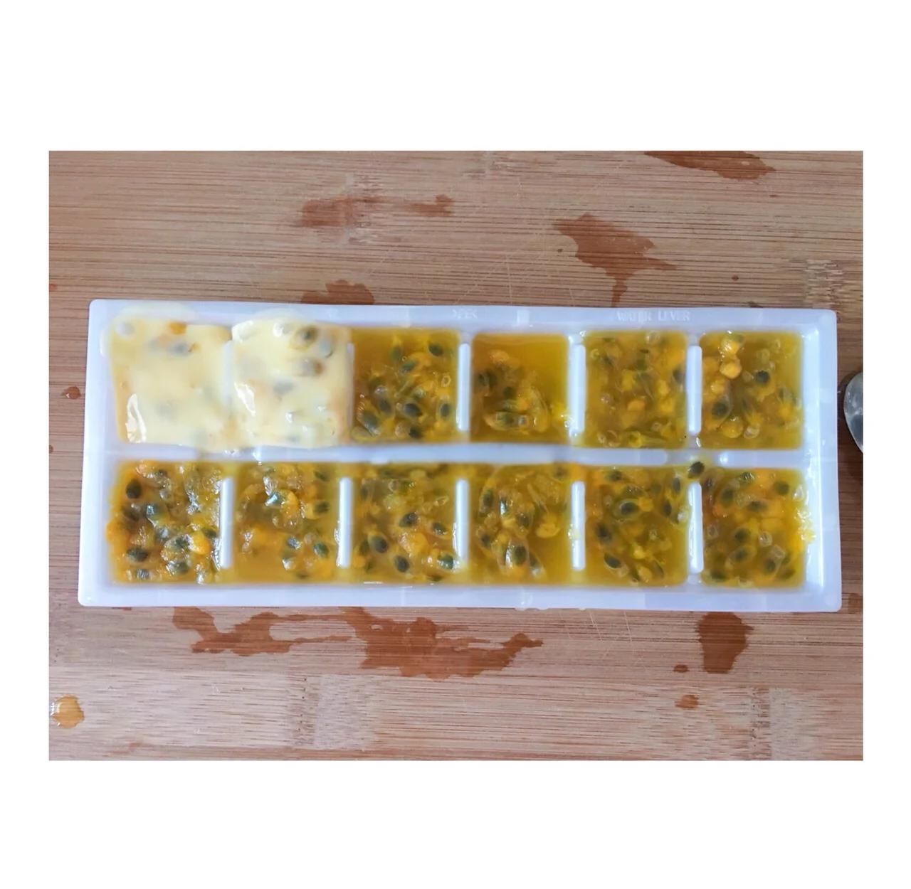 冰镇百香果牛奶昔特写：玻璃高脚杯中呈现自然紫白双色分层，表面浮着3颗晶莹冰块，杯壁凝结细密水珠，背景为木质料理台与两颗新鲜百香果