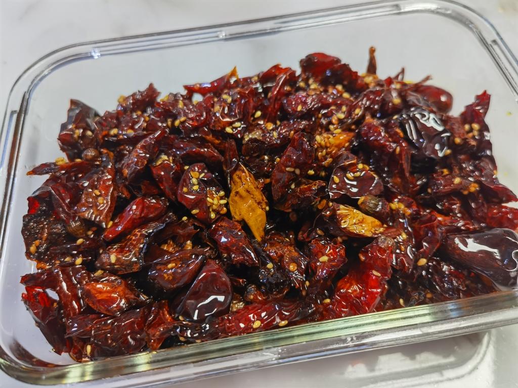 一碗自制辣椒油特写,油色红亮,表面漂浮着剪碎的干小米椒和白芝麻,旁边配有筷子和瓷碗 一碗自制辣椒油特写,油色红亮,表面漂浮着剪碎的干小米椒和白芝麻,旁边配有筷子和瓷碗
