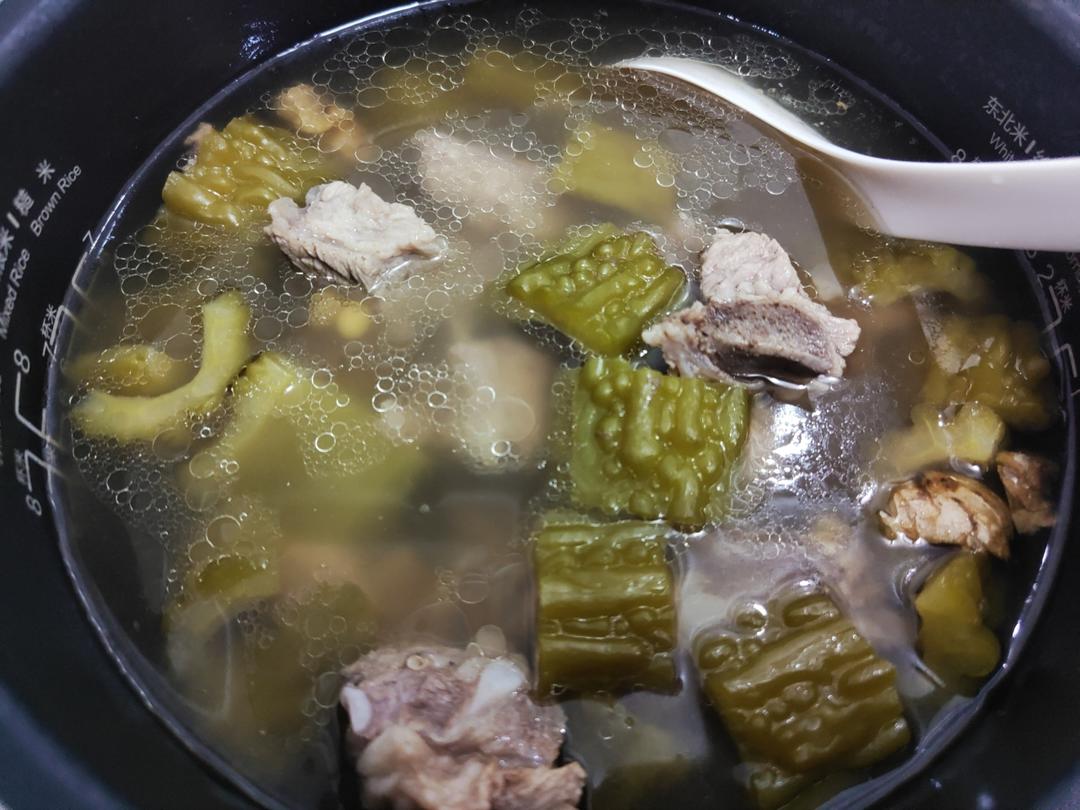 经期适宜食谱示范:苦瓜排骨汤实景图,突出温补食材搭配与安全烹饪场景,体现中医食养‘寒热平调’原则 女性手捧一碗热气腾腾的苦瓜排骨汤,汤色清亮微黄,可见苦瓜片与排骨块,旁边摆放生姜片与枸杞,背景为木质厨房台面