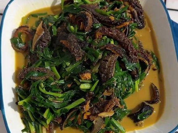 海参韭菜食材特写：案板上整齐摆放着晶莹Q弹的泡发辽参（表面无水光）、翠绿粗壮的头刀韭菜段（根白叶绿分明）、小葱白段、姜末与蒜片，背景为木质砧板与不锈钢盆