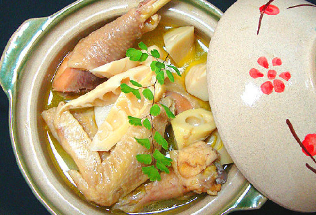 中式厨房灶台上,一口黑色铸铁锅正在慢火炖煮鸡肉烧竹笋,锅盖微启,热气升腾,锅内可见鸡肉与竹笋交融,旁边摆放着生姜、葱段等辅料,整体呈现温馨家常烹饪氛围 厨房灶台炖煮场景