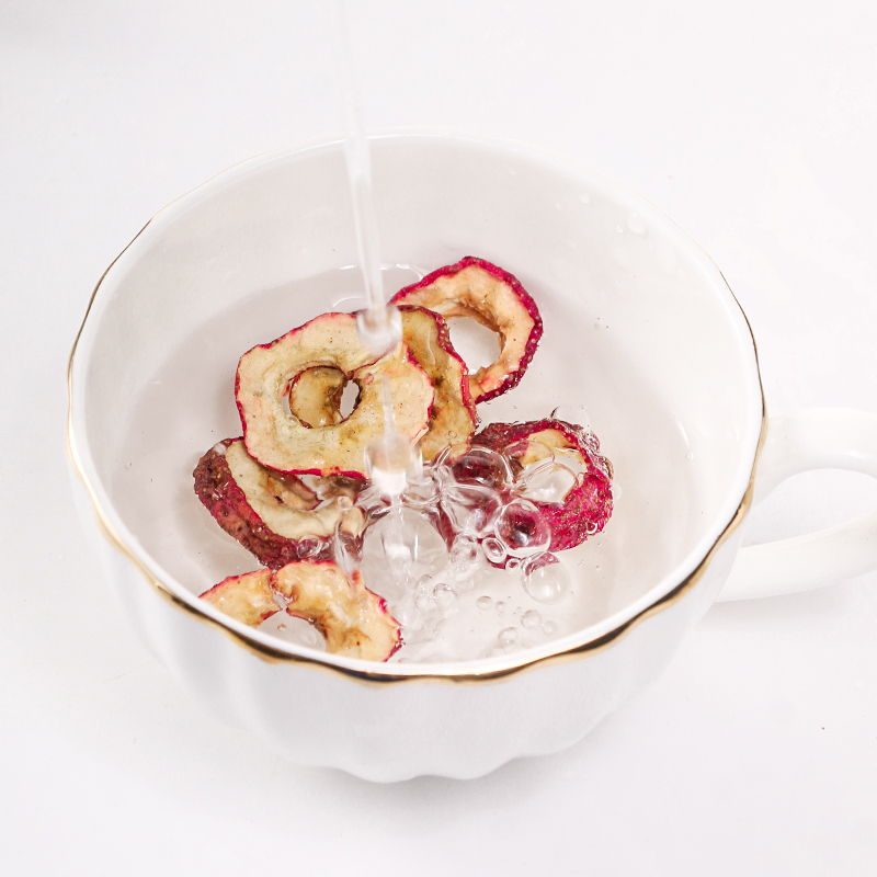 一杯清澈透亮的红枣干泡水放置在木桌上,水中浸泡着三片饱满的干红枣,液体呈现淡琥珀色,杯子旁摆放一枚完整的干红枣和一片切开的红枣片,背景虚化,突出饮品的自然与健康氛围 红枣干泡水成品展示