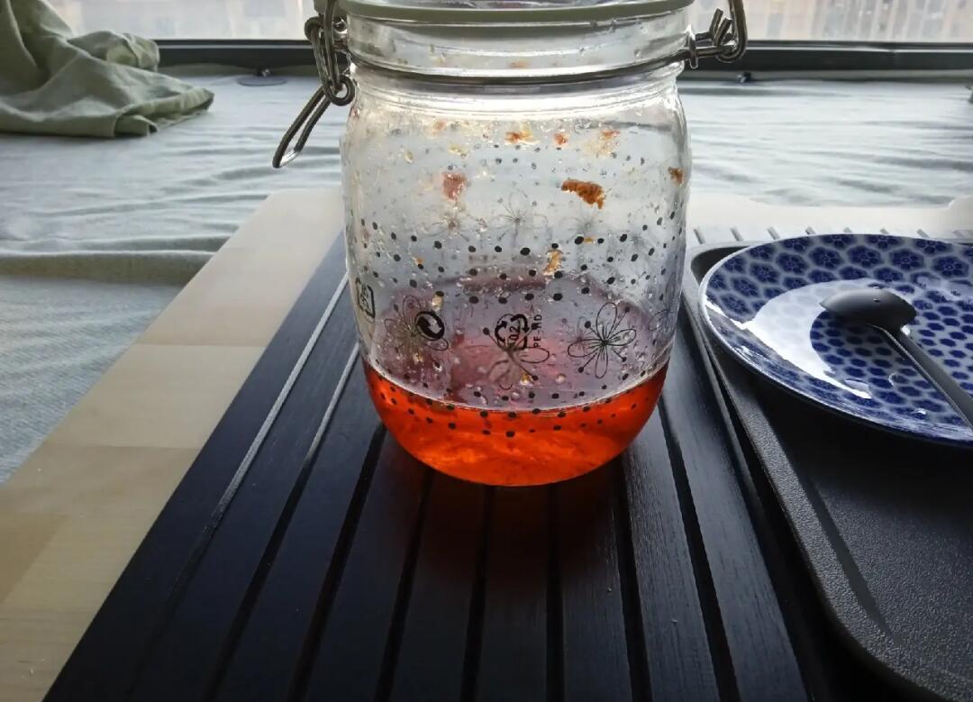 一个透明玻璃罐中盛放着深红色的车厘子果酱,表面光滑并反射光线,旁边放有一把木勺,背景为厨房台面,体现家庭加工场景 车厘子果酱制作过程中的玻璃罐装成品