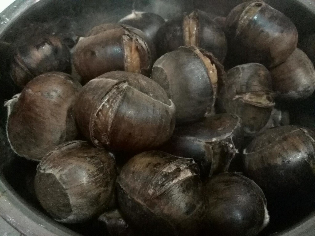 烤熟栗子特写：金棕色带光泽外壳，微微裂口露出淡黄色绵软果肉，置于竹编小筐中，背景为木质料理台与复古铜锅