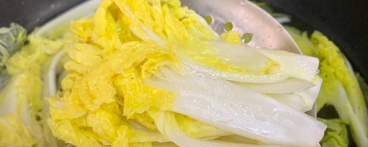 一位家庭主妇正在现代化厨房中烹饪上汤娃娃菜,不锈钢灶台上架着一口深色砂锅,锅内翻滚着浅黄色汤汁,其中漂浮着绿色的娃娃菜和红色枸杞,旁边摆放着切好的蒜片和调料瓶,环境整洁明亮 厨房制作过程场景