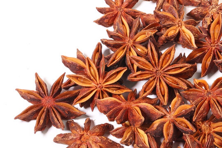 一颗完整的干燥八角茴香,呈深棕色星形结构,由八个左右的蓇葖果对称排列组成,表面有明显纹理,顶端可见鸟喙状尖头,背景为木质砧板,突出其天然农产品属性 八角茴香整体形态特写