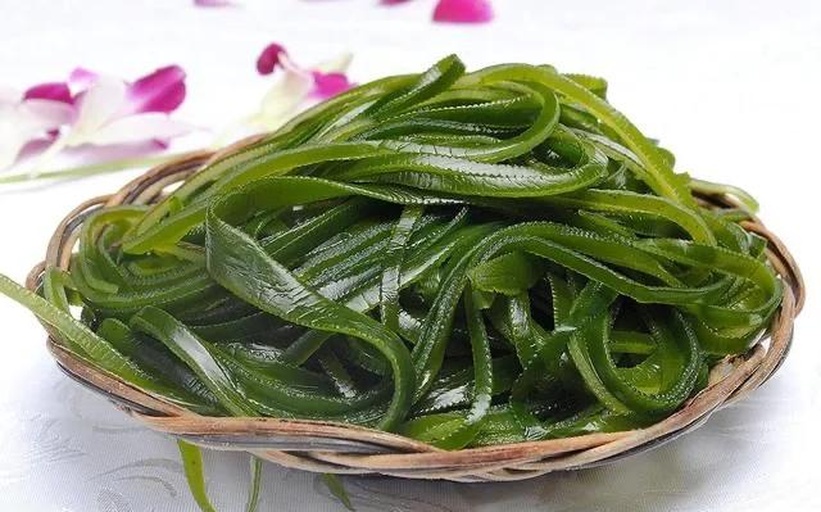 一束干燥的深褐色条状干海带平铺在木质桌面上,表面带有自然光泽和细微盐霜,背景为浅色厨房环境,突出食材原生态质感 干海带实物特写