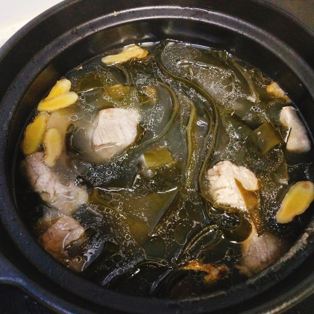 一碗热气腾腾的海带排骨汤,汤色乳白微黄,海带条与排骨段清晰可见,表面浮有少量油星,旁边配有姜片与葱花点缀,背景为木质餐桌与砂锅 海带排骨汤成品图