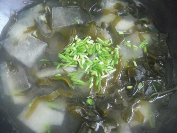 更年期女性厨房场景：青花瓷碗中盛放泡发好的淡干海带丝，搭配豆腐块与枸杞，汤面浮着几滴香油，旁边放着标有“山东荣成淡干海带（Laminaria japonica）”字样的食品级密封罐