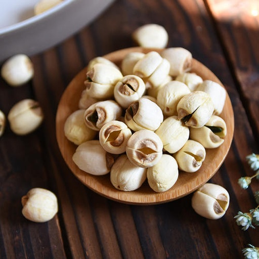 一盘散装的干燥白莲子,颗粒饱满,颜色为乳白色至淡黄色,表面光滑,背景为木质餐桌,旁边配有陶瓷碗和竹制小勺,突出天然健康食品的视觉氛围 白莲子特写