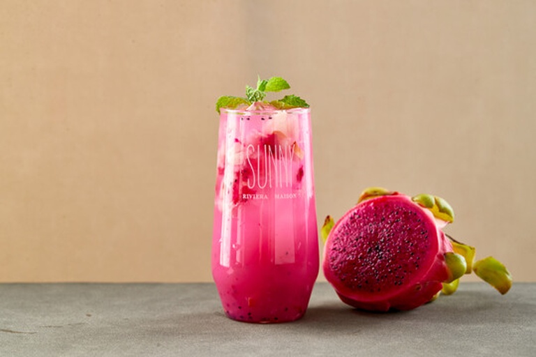 一杯透明玻璃杯中盛满粉紫色的火龙果酸奶汁,液体呈现丝滑质地,杯口点缀一片薄荷叶,杯子放在白色瓷盘上,背景为阳光洒入的厨房窗台,旁边放着半个空的火龙果壳 火龙果酸奶汁成品展示