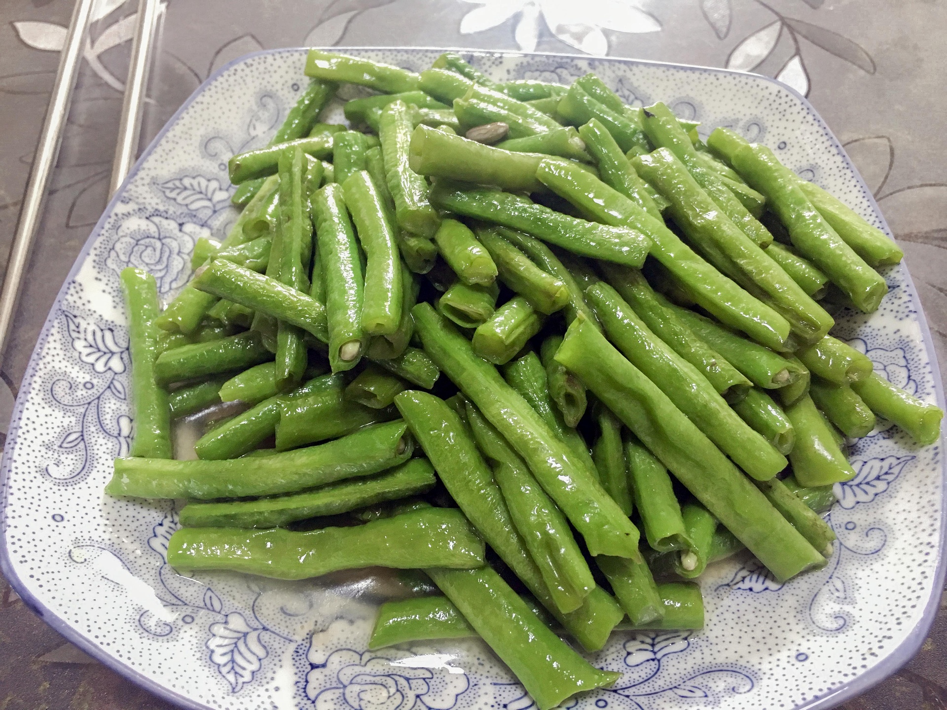 一盘刚出锅的白不老菜肴盛放在白色瓷盘中,豆角呈乳白色略带光泽,点缀着金黄蒜片和红色干辣椒,整体清爽诱人 白不老炒制完成装盘效果图