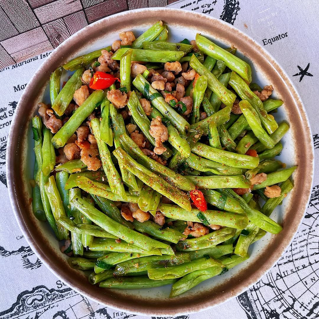 高清特写:琥珀色豆角段与焦香肉末交织,表面裹着透亮酱汁,点缀翠绿葱花与红亮野山椒,呈现诱人油亮光泽与丰富质感 泡椒豆角炒肉末出锅特写