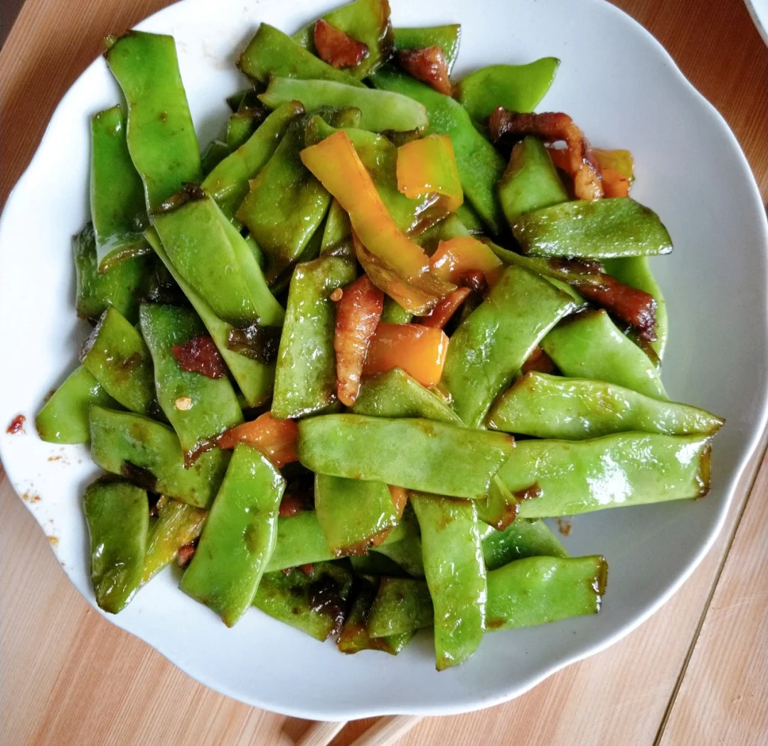 厨房灶台上正在翻炒的扁豆炒肉,锅中扁豆与肉片混合,肉片呈浅褐色,扁豆翠绿,锅气升腾,旁边摆放着切好的姜末和干辣椒,前景有酱油瓶和调料碗 扁豆炒肉过程图