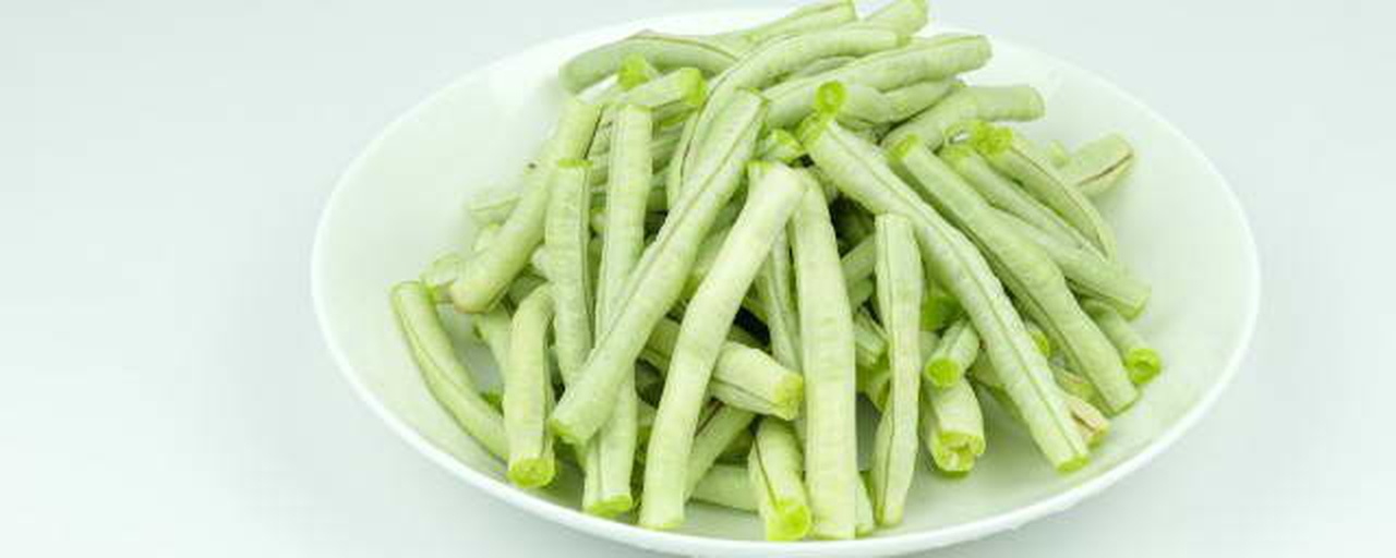 新鲜绿色长条状豆角与深绿色宽叶油菜并列摆放于白色瓷盘中,背景为厨房操作台,自然光照射,展现两种蔬菜的新鲜状态 豆角和油菜的实物对比图