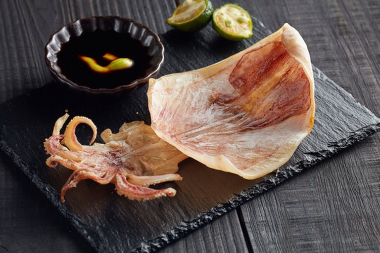 一盘晶莹剔透的生腌鱿鱼整齐码放在黑色石板上,周围点缀柠檬片和香菜叶,腌汁微微反光,整体呈现高级餐厅摆盘风格,背景虚化显示木质餐桌 成品展示