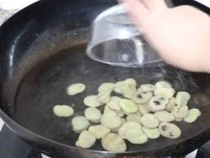 一位中老年人正在厨房用铁锅翻炒蚕豆