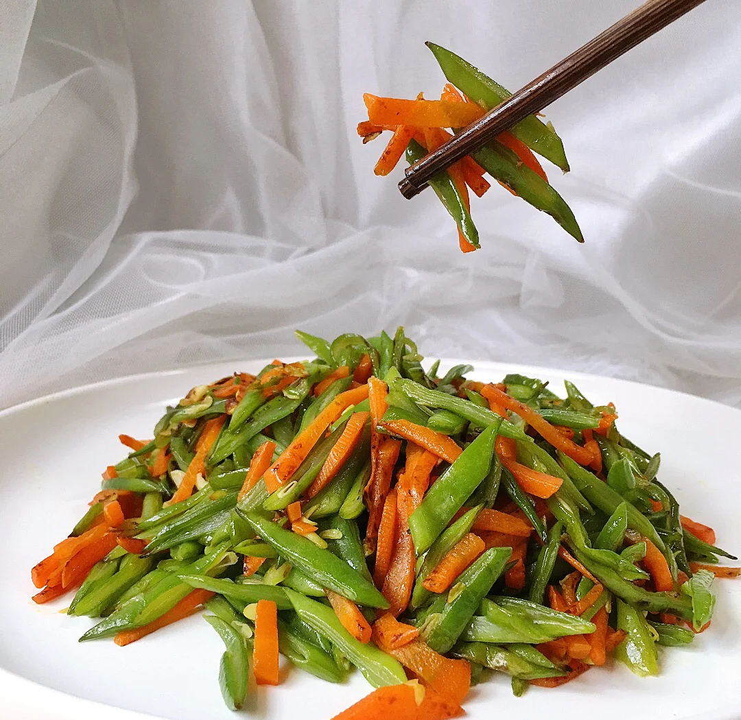 胡萝卜与四季豆切丝并列摆放于砧板，背景为不锈钢炒锅与木质锅铲，体现家常烹饪场景