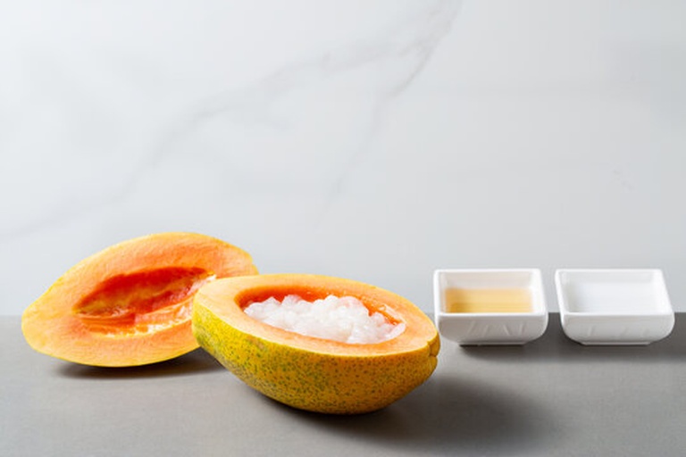 一张俯拍照片展示一整颗新鲜木瓜置于中央,周围摆放切好的果肉、干燥木瓜皮条、一瓶自制木瓜酵素饮料和一小碗木瓜皮炖汤;背景为浅色亚麻布,体现自然健康的饮食生活方式 木瓜整体与加工产品组合陈列