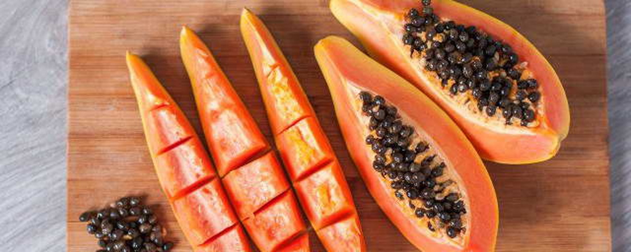 一个新鲜成熟的木瓜被横向切开,清晰展示橙红色的果肉与浅绿色略带斑点的外皮之间的分界线;背景为木质砧板,旁边放置一把不锈钢水果刀,强调食材的新鲜与可加工性 木瓜剖面图展示果肉与外皮结构