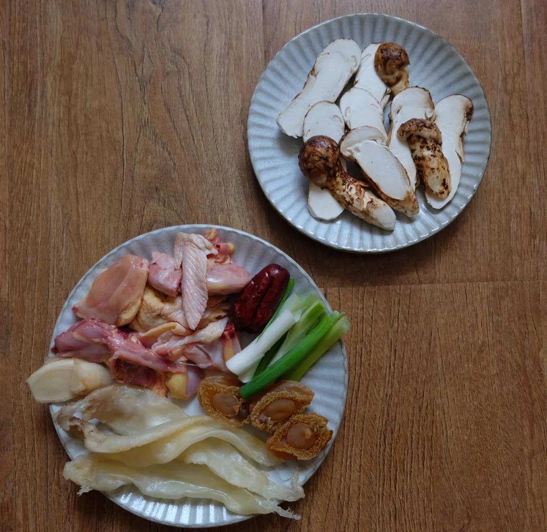 新鲜鸡肉块与干燥姬松茸、泡发后的姬松茸一同陈列在木砧板上,旁边有葱段、姜片等辅料,展示主要原材料准备状态 鸡肉与干/鲜姬松茸并列摆放于木质案板上,背景为厨房环境,光线柔和自然