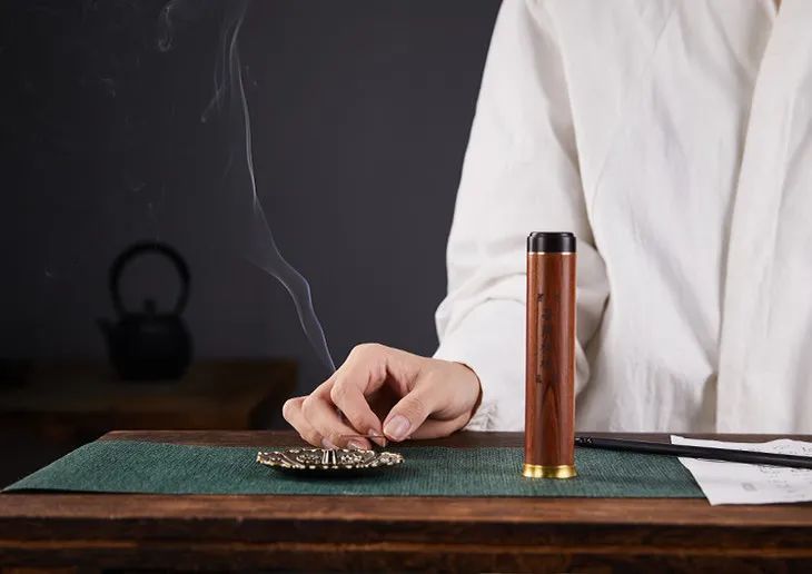 一位身着素色汉服的香道师坐在木案前,手中持银匙搅拌陶罐中的沉香与梨块混合物,罐口热气升腾,周围摆放着梨子、香料、竹制工具等,背景为中式茶室,氛围静谧庄重 现代香道师正在制作鹅梨帐中香的工艺过程