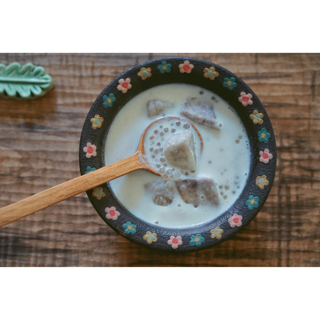 一张木制餐桌上摆放着一碗紫色香芋糯米丸子甜汤,旁边配有瓷勺和绿植装饰,整体氛围温暖舒适,体现家常美食的幸福感 家庭餐桌上的香芋甜品拼盘