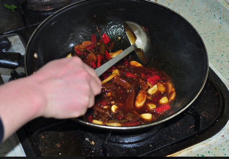 黑色不粘炒锅置于燃气灶上,炉火调至最小,锅内浅层食用油中漂浮着细碎蒜蓉,呈现金黄色泽,厨师手持木铲轻轻搅动;锅旁摆放玻璃调料碗,内含已混合的生抽、蚝油和白糖,背景可见酱油瓶与计量勺,突出蒜蓉酱汁制作过程 炒锅中小火加热的蒜蓉正在金黄色油中翻滚,锅边放置酱油瓶和小碗调料