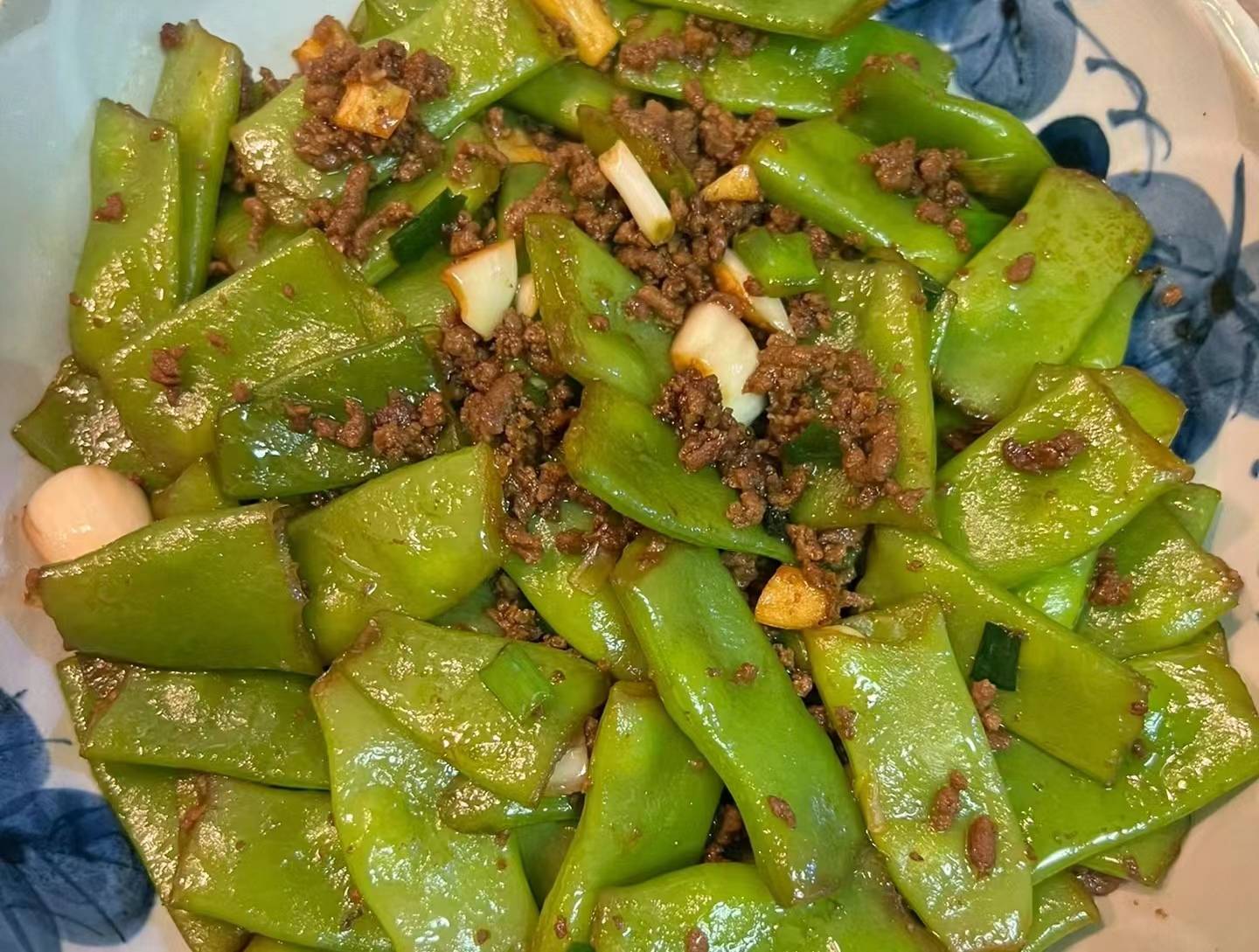一个家庭厨房场景,砧板上放着新鲜的绿色扁豆,旁边有切好的蒜末,锅中正在翻炒扁豆,热气腾腾,体现日常烹饪的真实感 厨房中烹饪扁豆的场景