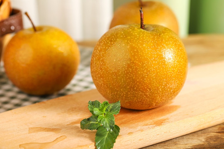 黄金梨切开展示图：横切面果肉雪白细腻、果核小、汁水欲滴，背景为竹制砧板与不锈钢水果刀，侧光凸显果肉半透明质感与丰富汁囊结构