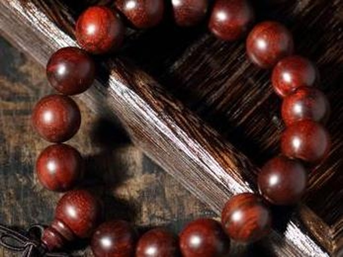 一串打磨光亮的金花梨佛珠手链平铺在黑色绒布上,珠子呈金黄色带深褐条纹,表面反光细腻;旁边放置一个放大镜,镜片下可见木材导管分布均匀,呈现典型的热带硬木微观结构特征 金花梨手串与放大镜对比图